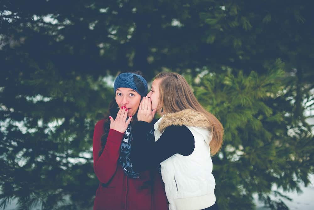 woman whispering in other woman&rsquo;s ear